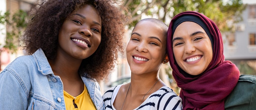Three women smiling together outdoors, representing connection and community among Community Health Workers.